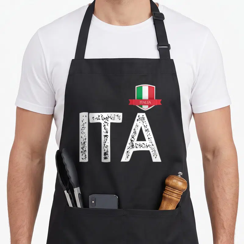Tablier de cuisine noir avec les lettres ITA en blanc texturé et un écusson au drapeau italien portant l'inscription ITALIA.