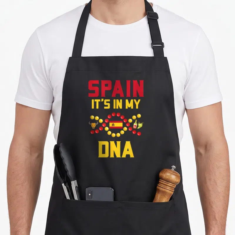 Tablier de cuisine noir avec l'inscription Spain it's in my DNA et des symboles espagnols colorés sur le devant.