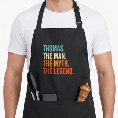Tablier de cuisine noir avec l'inscription colorée Thomas The Man The Myth The Legend en typographie vintage.