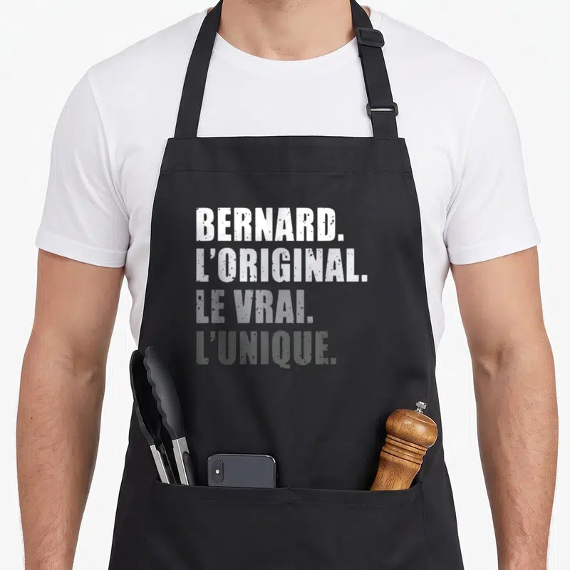 Tablier de cuisine noir avec inscription typographique blanche et grise proclamant Bernard l'original le vrai unique.