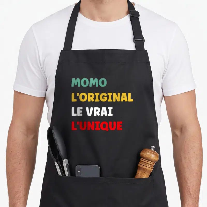 Tablier de cuisine noir avec les mots MOMO LORIGINAL LE VRAI LUNIQUE imprimés en couleurs vives.