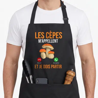 Tablier de cuisine noir avec illustration de cèpes et texte Les Cèpes m'appellent et je dois partir en orange et blanc.