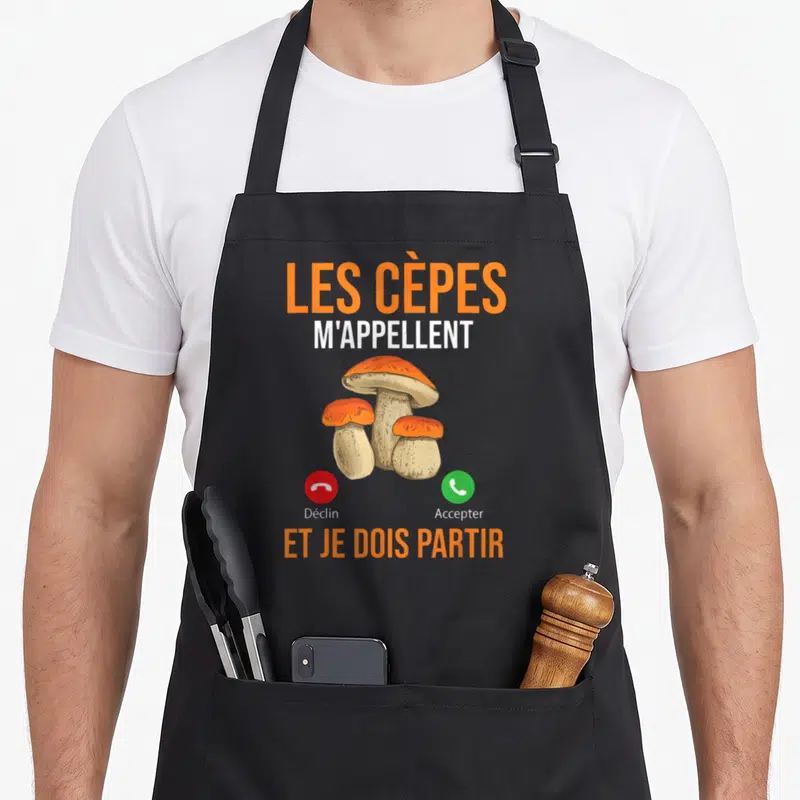 Tablier de cuisine noir avec illustration de cèpes et texte Les Cèpes m'appellent et je dois partir en orange et blanc.