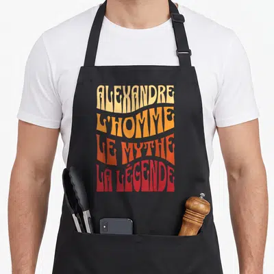 Tablier de cuisine noir avec inscription colorée Alexandre l'homme le mythe la légende en lettres ondulées.