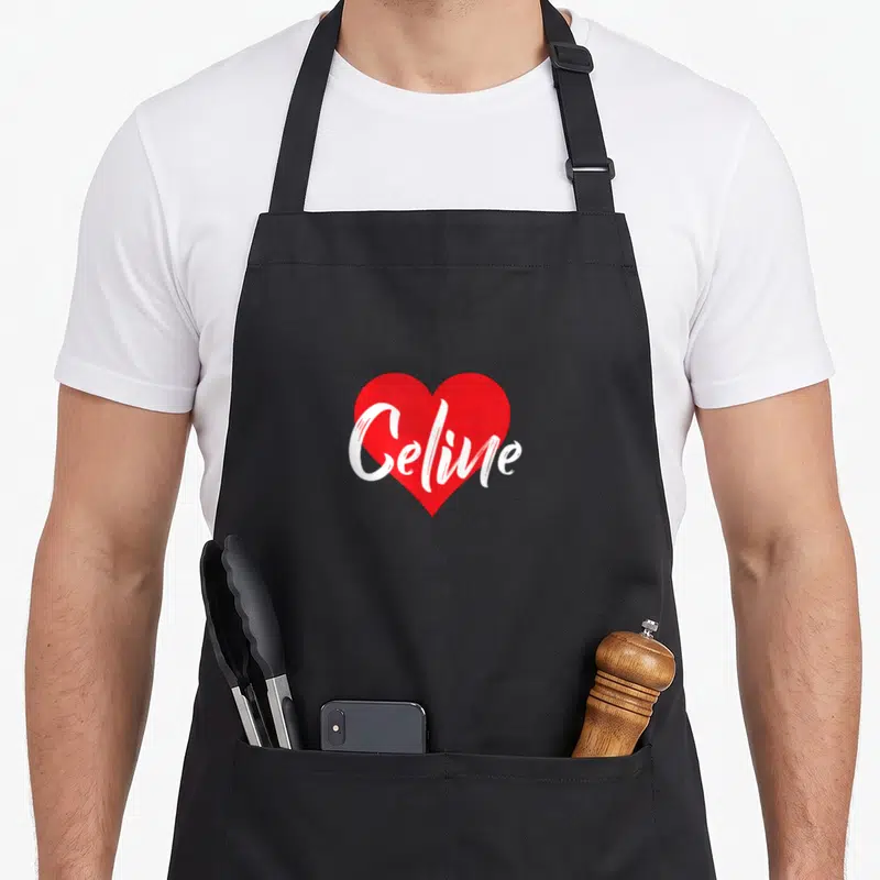 Tablier de cuisine noir avec un grand cœur rouge et le prénom Celine en blanc au centre.