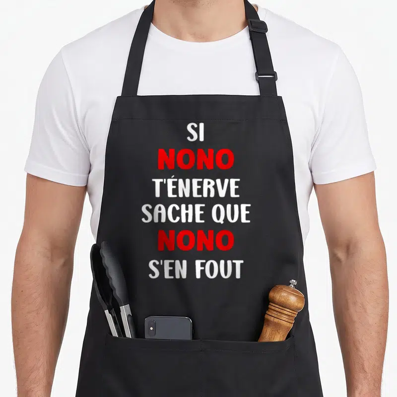 Tablier de cuisine noir avec le texte Si Nono t'énerve sache que Nono s'en fout en lettres blanches et rouges.