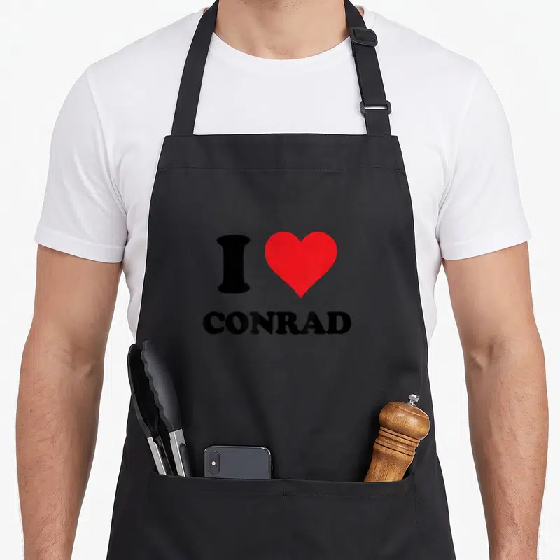 Tablier de cuisine noir avec un grand cœur rouge et le texte I Love Custom Stuff Conrad imprimé en noir au centre.