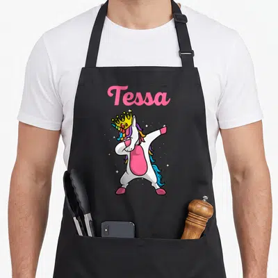 Tablier de cuisine noir avec une licorne royale faisant le dab et le prénom Tessa en rose.