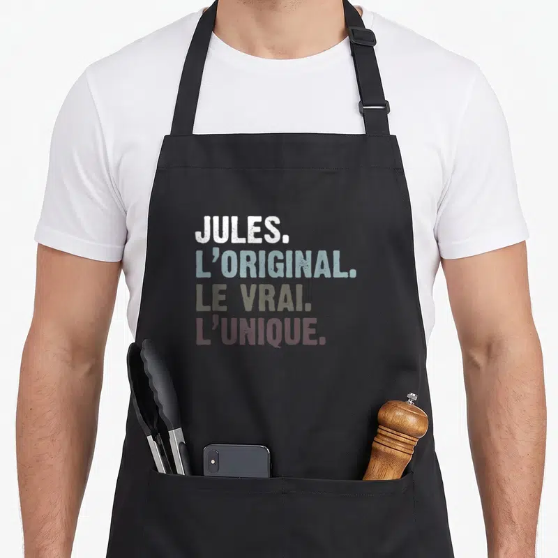 Tablier de cuisine noir avec les mots Jules l'original le vrai et l'unique imprimés en typographie colorée et décontractée.