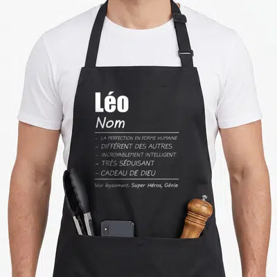 Tablier de cuisine noir avec l inscription Léo Nom et une liste d attributs humoristiques en blanc sur fond uni.