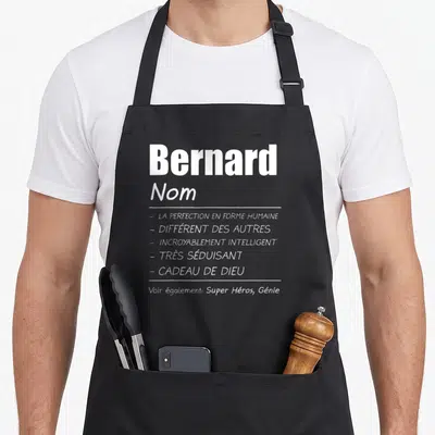 Tablier de cuisine noir avec le prénom Bernard et des qualificatifs humoristiques imprimés en typographie blanche contrastante sur le devant.