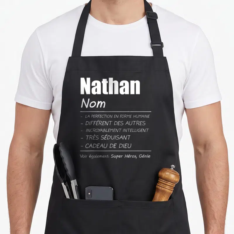 Tablier de cuisine noir avec le prénom Nathan et une liste d'attributs honorifiques imprimés en blanc au centre du vêtement.