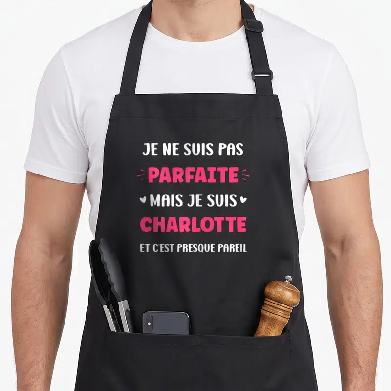 Tablier de cuisine noir avec la citation Je ne suis pas parfaite mais je suis Charlotte en typographie rose et blanche.