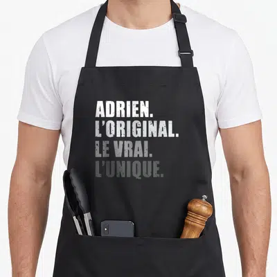 Tablier de cuisine noir avec inscription blanche et grise Adrien Loriginal Le Vrai Lunique en typographie délavée.