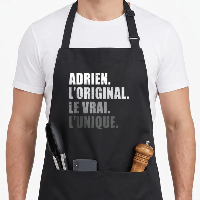 Tablier de cuisine noir avec inscription blanche et grise Adrien L'original Le Vrai L'unique en typographie délavée.