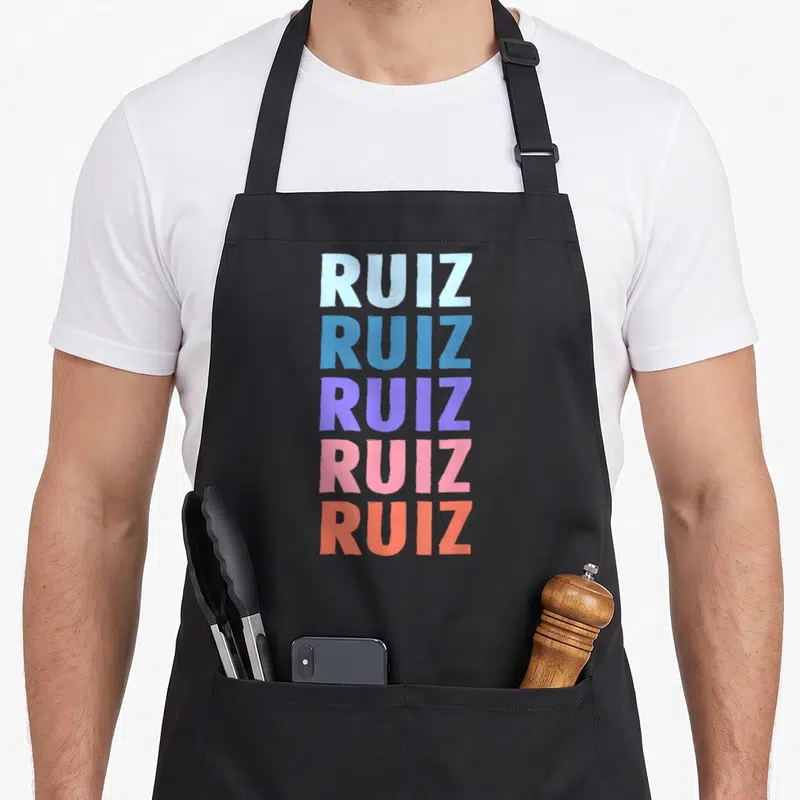 Tablier de cuisine noir avec le mot Ruiz répété cinq fois dans des teintes bleu, violet, rose et orange.