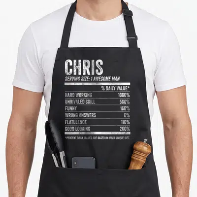Tablier de cuisine noir avec étiquette nutrition personnalisée au nom Chris et valeurs humoristiques en blanc.