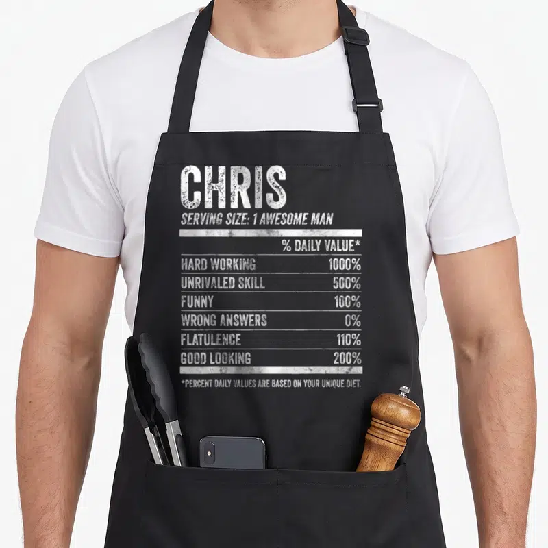 Tablier de cuisine noir avec étiquette nutrition originale au nom Chris et valeurs humoristiques en blanc.