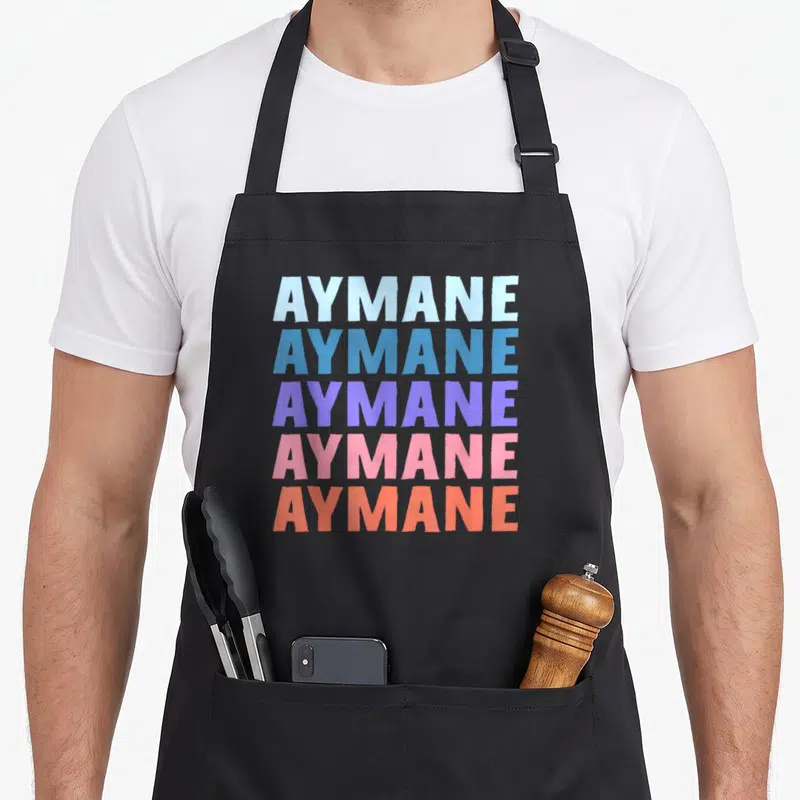 Tablier de cuisine noir avec le nom AYMANE répété cinq fois en lettres majuscules aux couleurs pastel et vives.