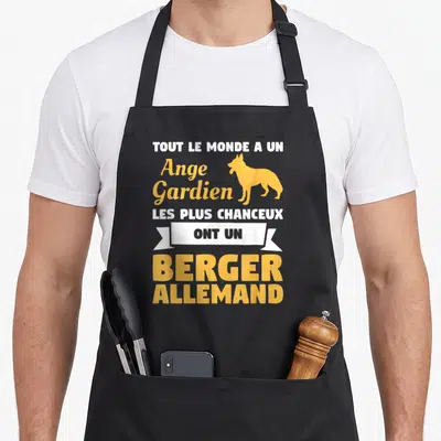 Tablier de cuisine noir avec texte blanc et jaune et silhouette de berger allemand debout sur fond uni.