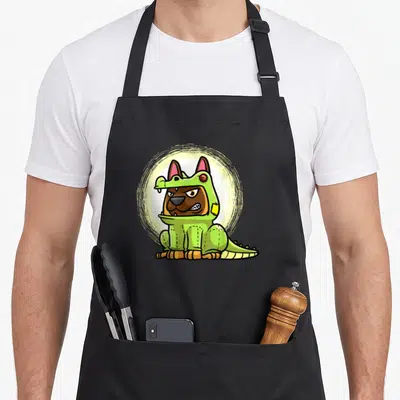 Tablier de cuisine noir avec illustration d'un chien Malinois portant un déguisement d'alligator vert sur fond circulaire jaune pâle.