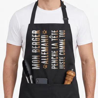 Tablier de cuisine noir avec texte vertical doré mon berger allemand penche la tête juste comme toi et deux empreintes de pattes.
