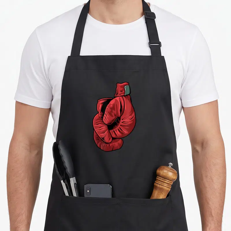 Tablier de cuisine noir avec illustration de gants de boxe rouges croisés en style dessin animé.