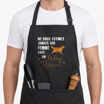 Tablier de cuisine noir avec l'inscription Ne sous-estimez jamais une femme avec un Golden Retriever et une illustration du chien en marche.