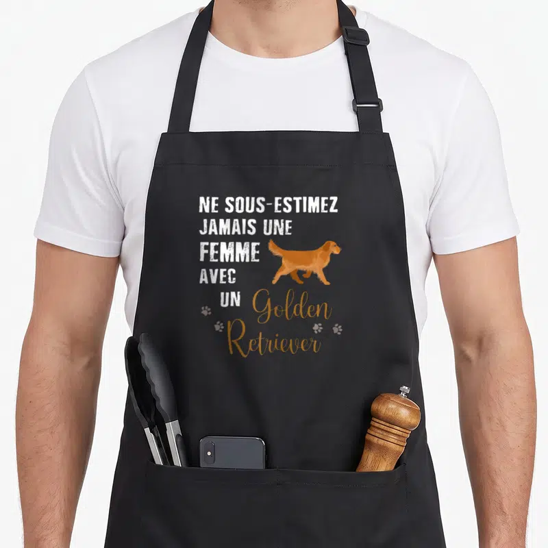 Tablier de cuisine noir avec l'inscription Ne sous-estimez jamais une femme avec un Golden Retriever et une illustration du chien en marche.