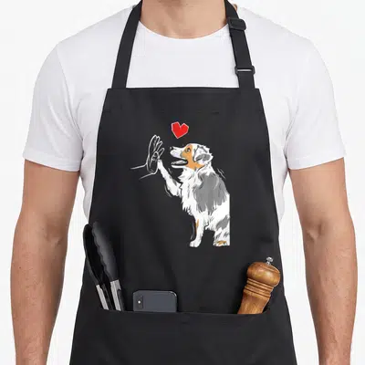 Tablier de cuisine noir avec illustration d'un chien Berger Australien faisant un high five sous un cœur rouge stylisé.