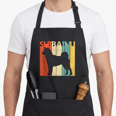 Tablier de cuisine noir avec silhouette grise Shiba Inu et texte SHIBAINU sur bandes colorées orange, crème, turquoise et jaune.