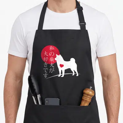 Tablier de cuisine noir avec silhouette blanche de chien Shiba Inu, cœur rouge et cercle rouge portant des caractères japonais blancs.