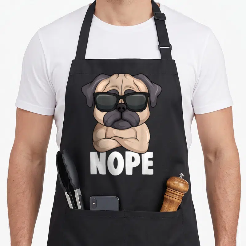 Tablier de cuisine noir avec illustration d'un carlin musclé portant des lunettes noires et le texte NOPE en blanc.