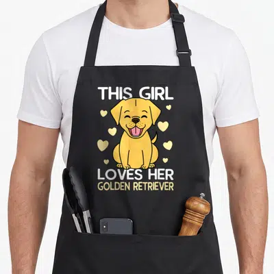 Tablier de cuisine noir avec un chiot golden retriever souriant et le texte This Girl Loves Her Golden Retriever.