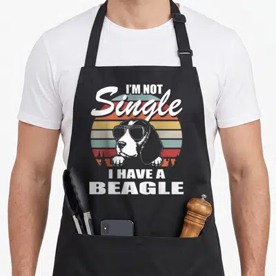 Tablier de cuisine noir avec illustration d'un beagle aux lunettes de soleil et texte en anglais sur fond coloré vintage.