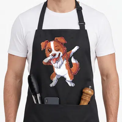 Tablier de cuisine noir avec illustration d'un chien Border Collie marron et blanc en train de faire une pose de danse ludique.