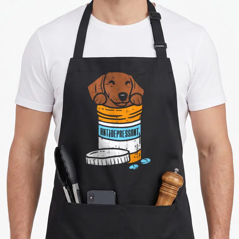 Tablier de cuisine noir avec illustration d'un teckel sortant d'un flacon Antidepressant orange et bleu.