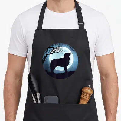 Tablier de cuisine noir avec illustration circulaire d'un chien face à la lune et un arbre aux branches nues.