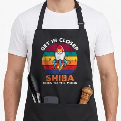 Tablier de cuisine noir avec un Shiba Inu dans une fusée et le texte Shiba goes to the moon sur fond arc-en-ciel rétro.