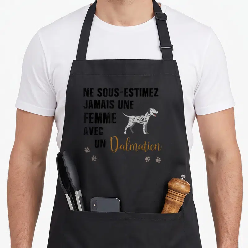 Tablier de cuisine noir avec inscription Ne sous-estimez jamais Le Pouvoir d'une Femme avec un Dalmatien et des traces de pattes orange.