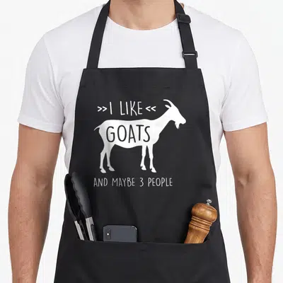 Tablier de cuisine noir avec silhouette blanche de chèvre et texte « I like goats and maybe 3 personnes » imprimé au centre.