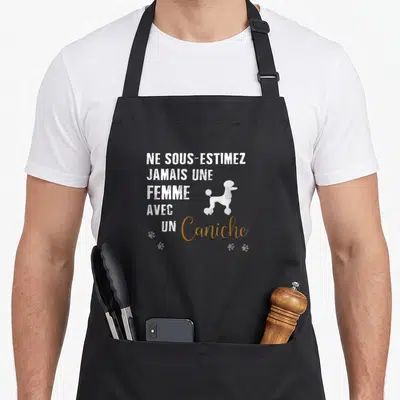 Tablier de cuisine noir avec l'inscription Ne sous-estimez jamais une femme avec un caniche et une illustration de chien blanc.