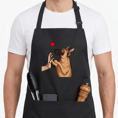 Tablier de cuisine noir avec illustration d'un chien Malinois tenant une main humaine sous un petit cœur rouge vif.