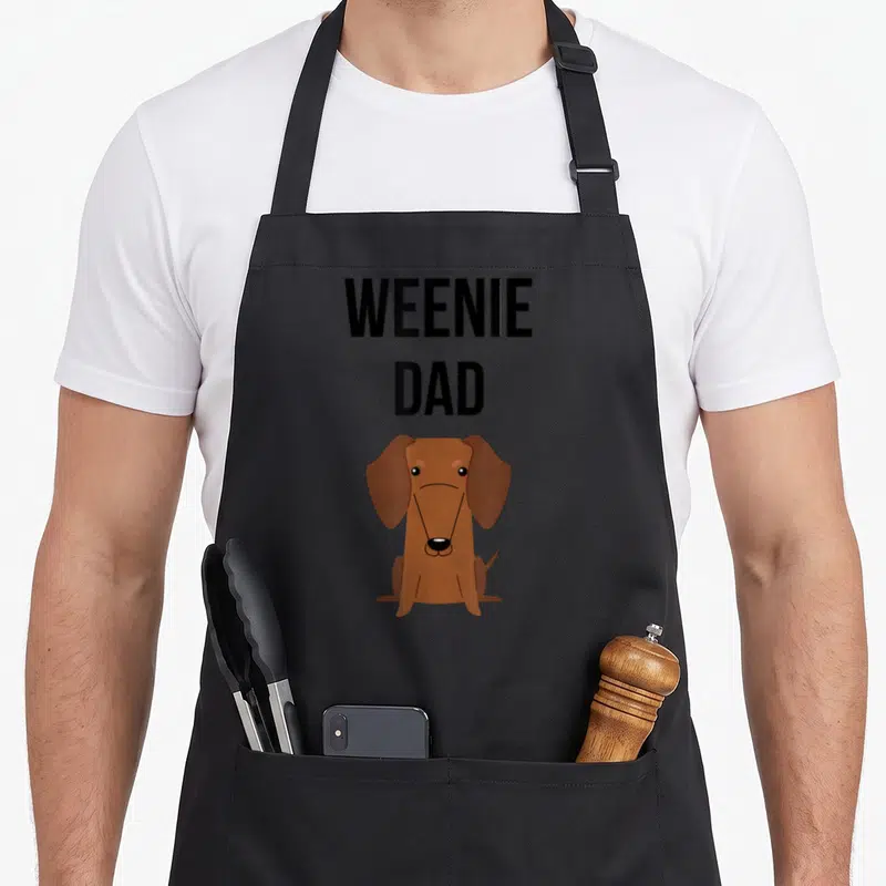 Tablier de cuisine noir avec illustration teckel marron et texte Weenie Dad en lettres noires.