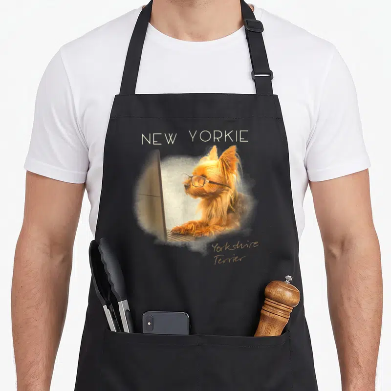 Tablier de cuisine noir avec un New Yorkie Smart portant des lunettes face à un écran d'ordinateur.