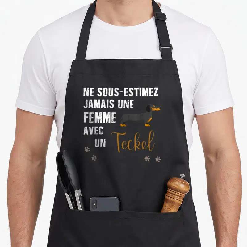 Tablier de cuisine noir avec l'inscription Ne sous-estimez jamais une femme avec un Teckel et un dessin de chien.