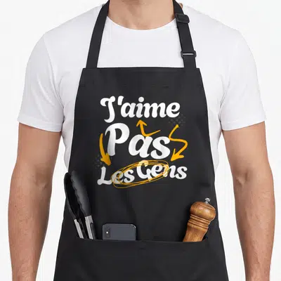 Tablier de cuisine noir avec inscription J'aime pas les gens en blanc et flèches oranges.