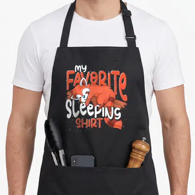 Tablier de cuisine noir avec illustration panda roux dormant et texte My Favorite Sleeping Shirt en orange et blanc.