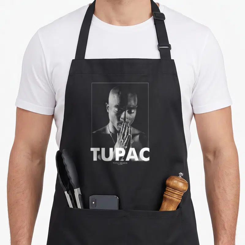 Tablier de cuisine noir avec portrait monochrome de Tupac Shakur et le mot TUPAC en blanc.