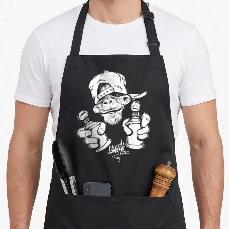 Tablier de cuisine noir avec un singe graffiti tenant deux bombes de peinture et le mot GRAFFITI imprimé en bas.